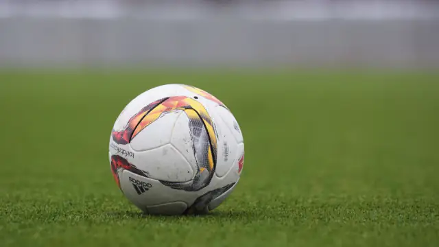 Bola de futebol pousada sobre um relvado, com fundo desfocado